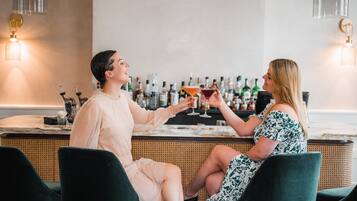 Deux personnes sont assises au bar, et on peut voir une variété de bouteilles en arrière-plan.