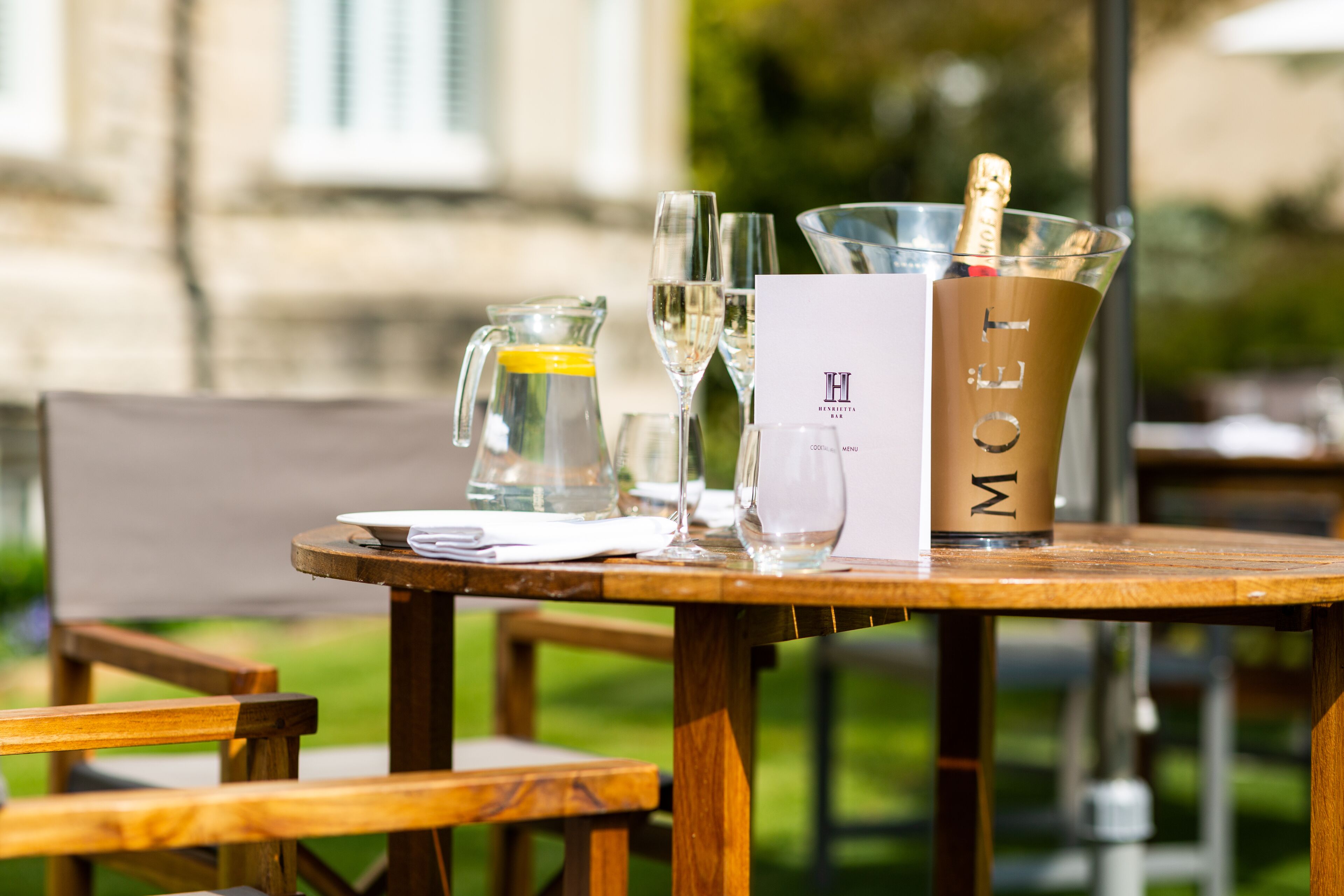 A table with a menu, a glass pitcher, a glass of water, a glass of wine, and a bottle of champagne.