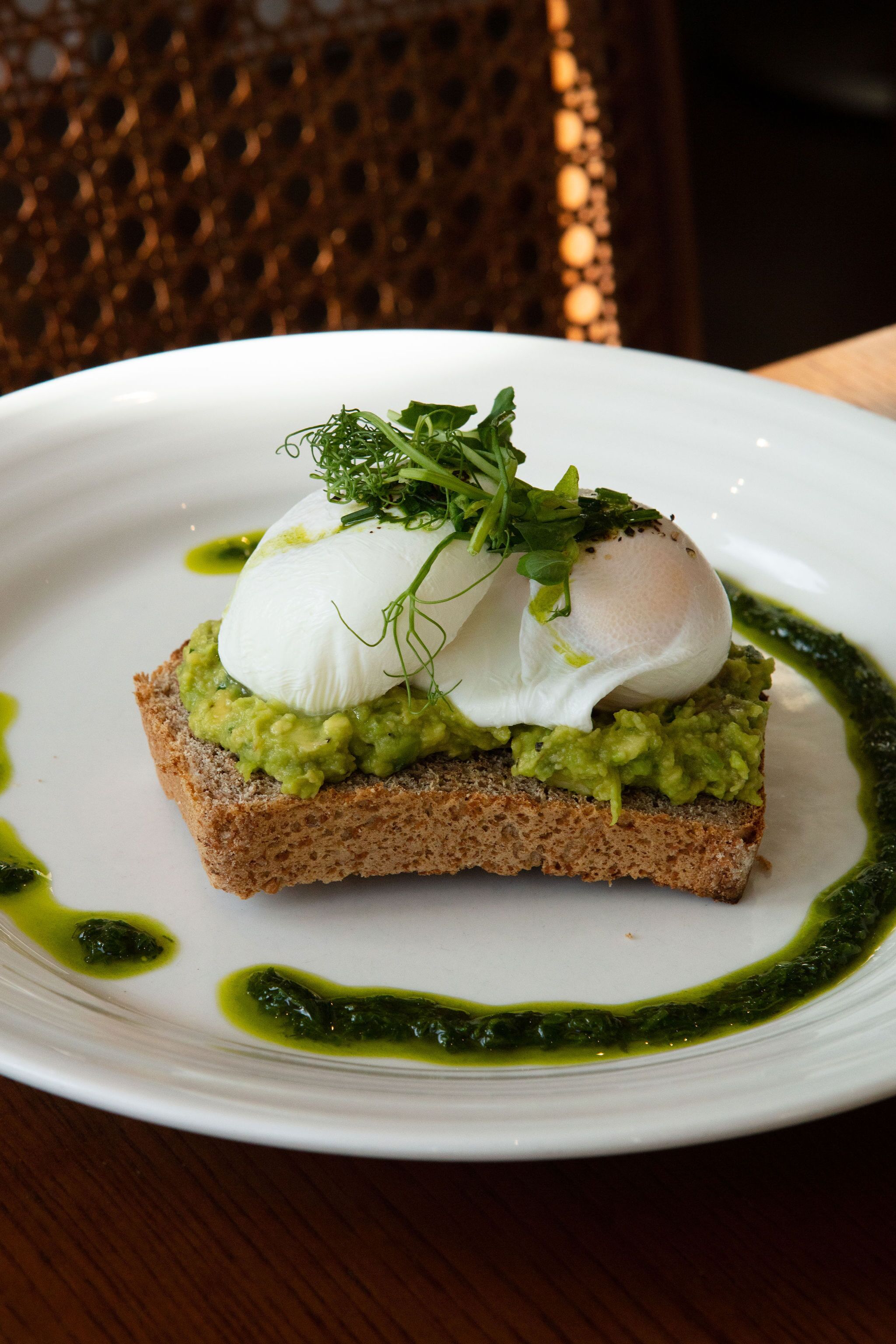 Un plato con una rebanada de pan cubierta de aguacate, un huevo escalfado y un chorrito de salsa verde.