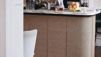Una zona de bar con un cantinero preparando bebidas, un espejo y diferentes botellas y frutas sobre la barra.