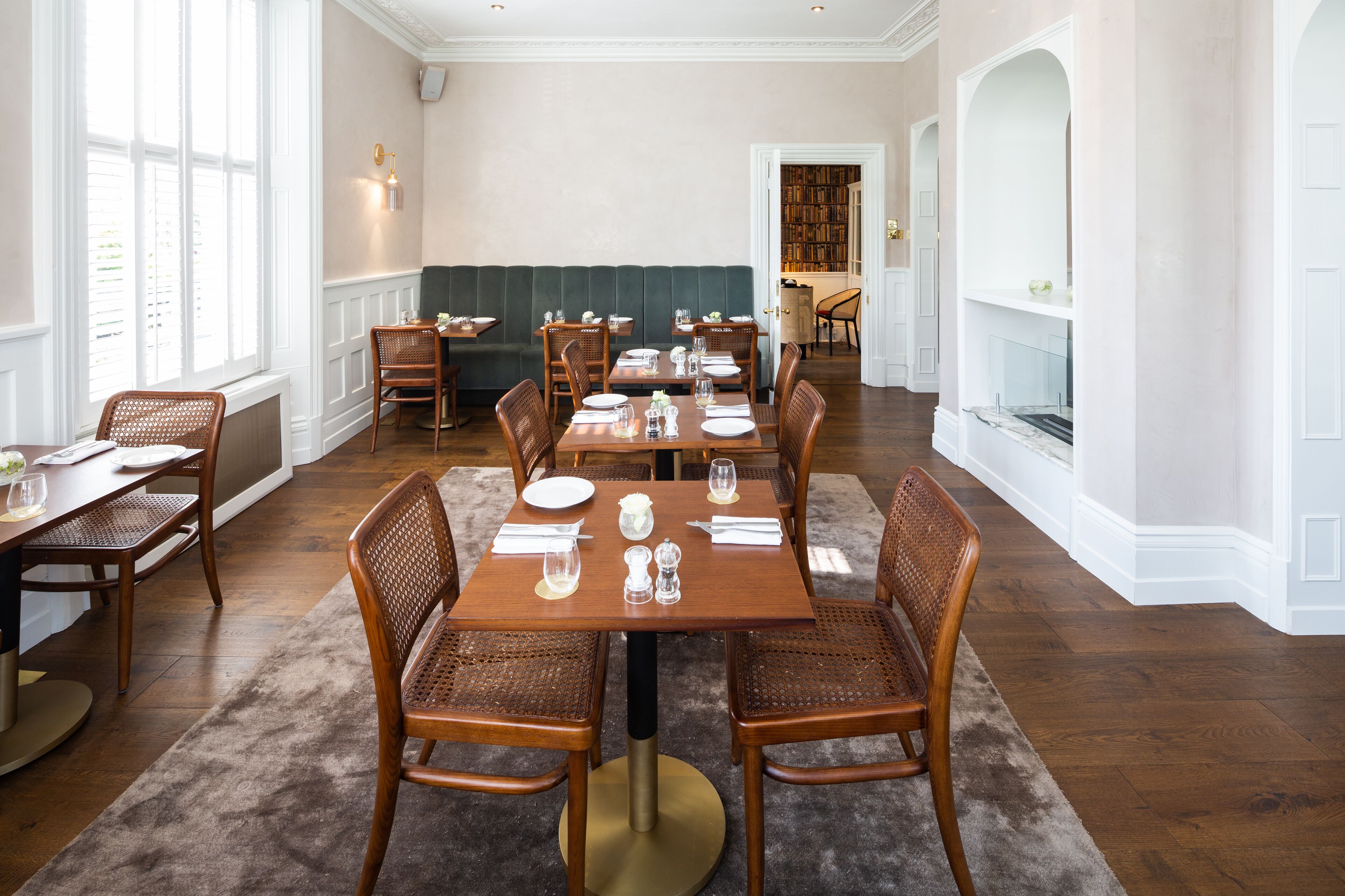 A dining area with a long table set for six, surrounded by wicker chairs. A green upholstered bench is visible in the background.