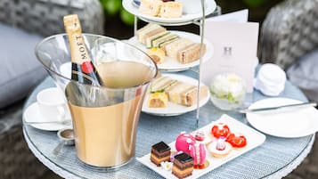 A glass table with a bottle of champagne, a tiered dessert stand, and various pastries.