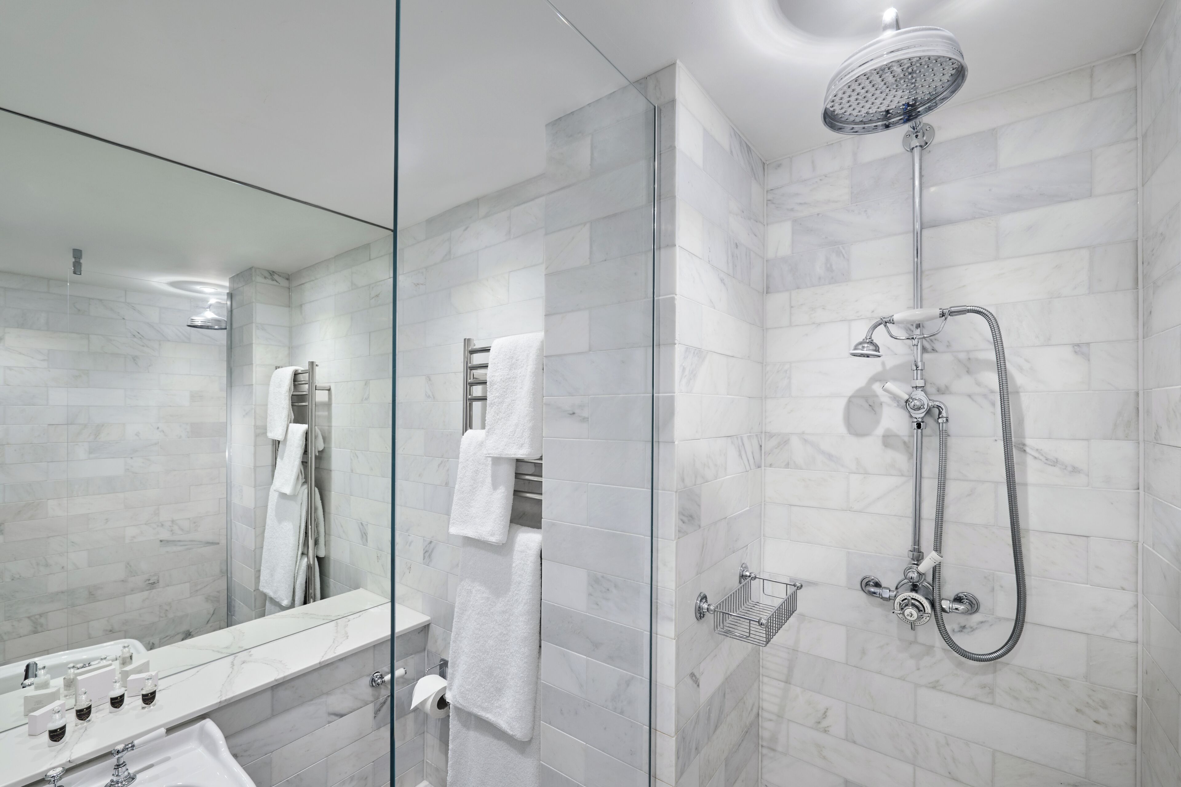 A modern bathroom with a glass shower enclosure, a marble-tiled shower area, a glass-enclosed vanity with a sink, and a mirror.