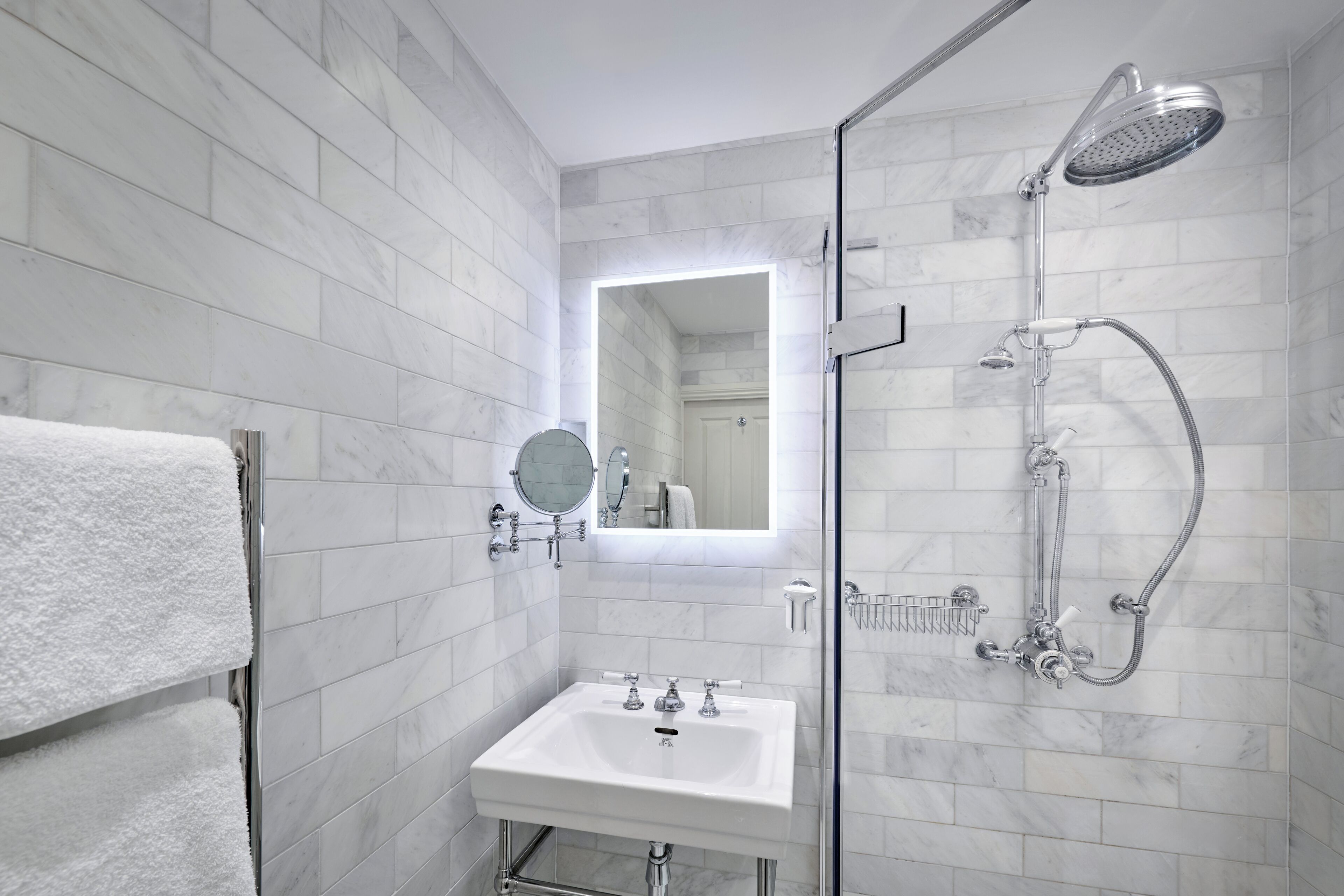 Un baño moderno con ducha envuelta en vidrio, un lavamanos blanco y un espejo sobre él.