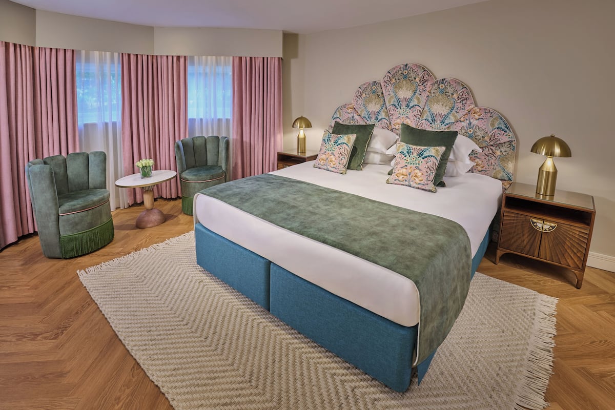 A bedroom with a large bed, two chairs, a small table, and a nightstand with lamps.