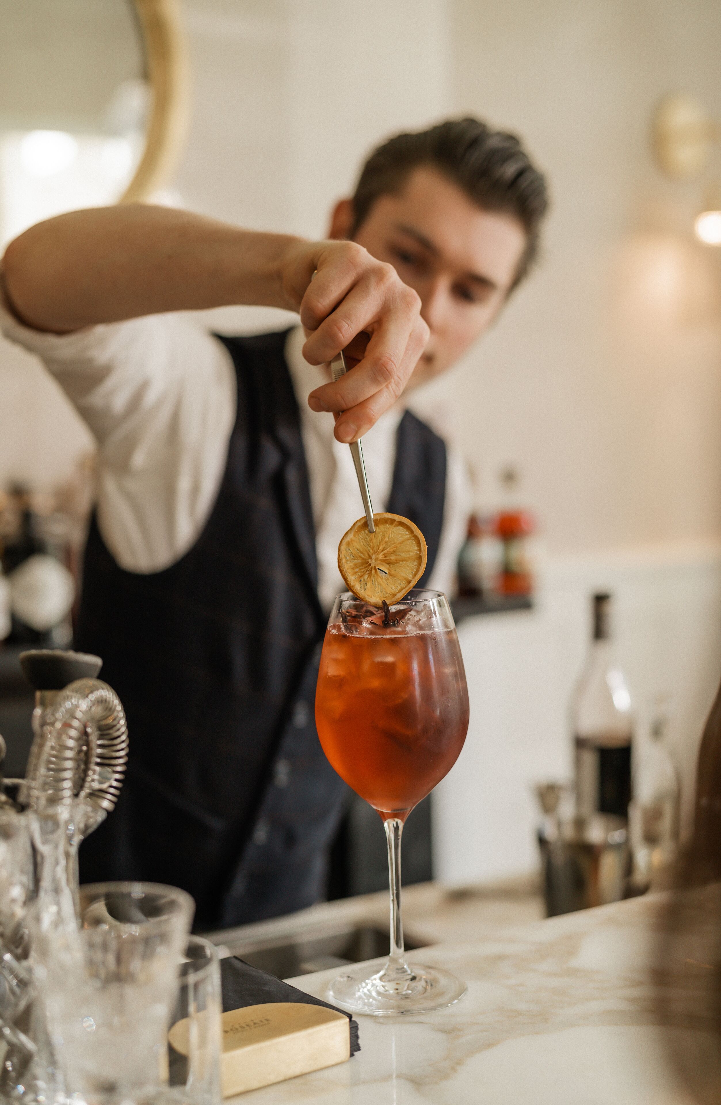 A bartender preparing a cocktail with a garnish in a glass.