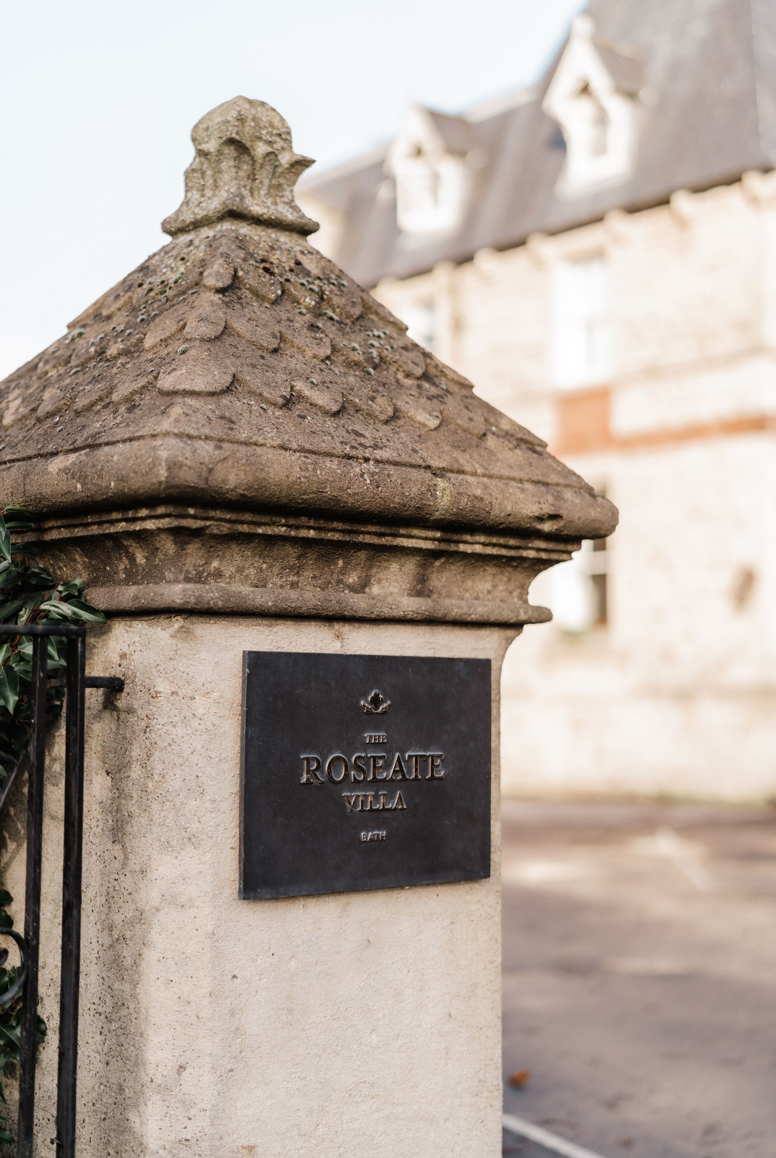 A stone pillar with a plaque reading "The Roseate Villa" and a decorative stone roof.
