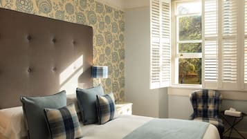A bedroom with a tufted headboard, a bed with plaid bedding, a nightstand, a chair, and a window with shutters.