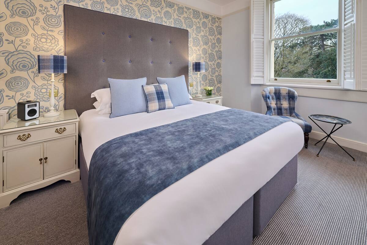 A neatly arranged bedroom with a large bed, bedside lamps, a small table, and a chair.