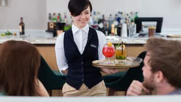 Un barman sert des boissons aux clients dans un bar, avec un comptoir et diverses bouteilles en arrière-plan.