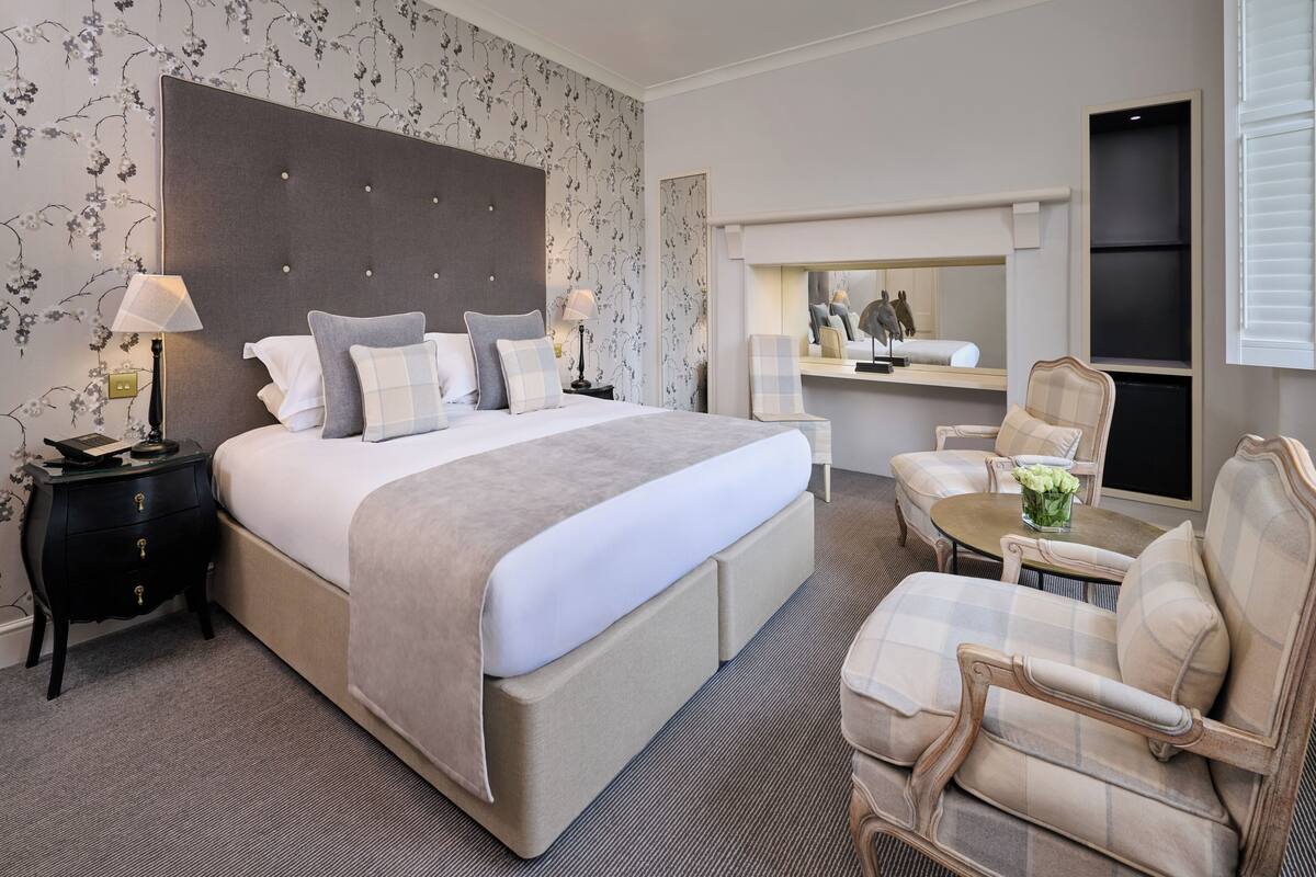 A hotel room with a large bed, two bedside tables, a chair, a small table, and a mirror.