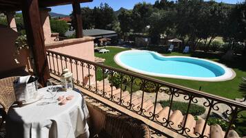 Un balcon donnant sur une piscine, avec des meubles d’extérieur et une table dressée pour un repas.