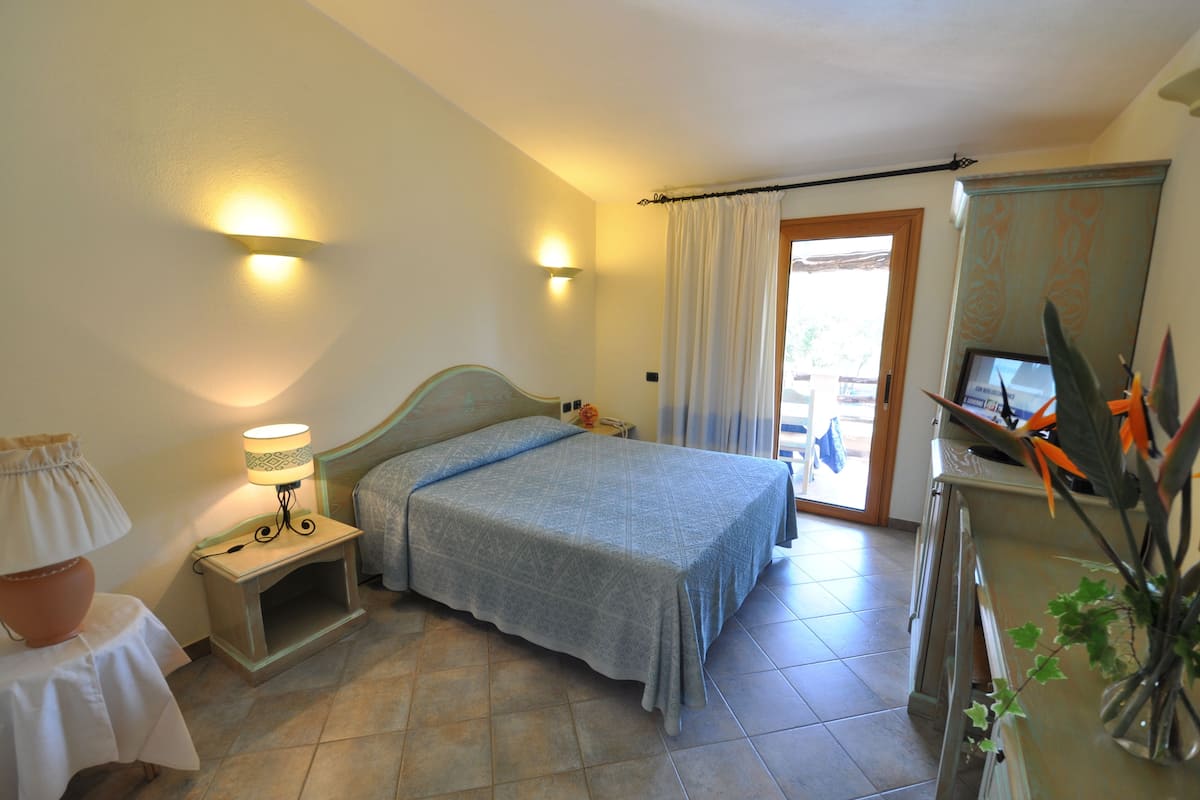 Ein Schlafzimmer mit Bett, Nachttischlampe und Schreibtisch mit Computer.