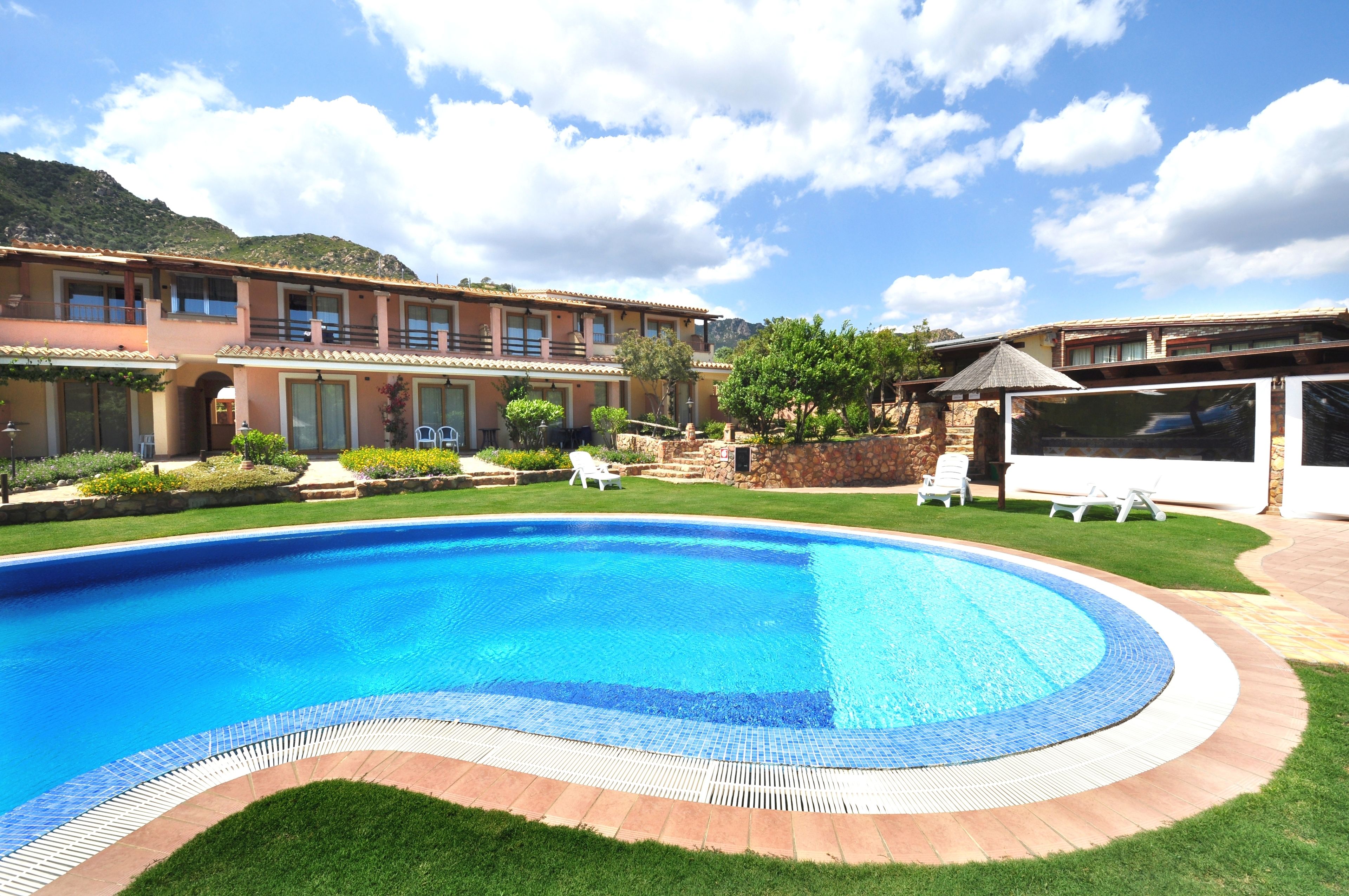Una piscina con borde de azulejos, rodeada por un césped cuidado y un edificio con varios balcones.