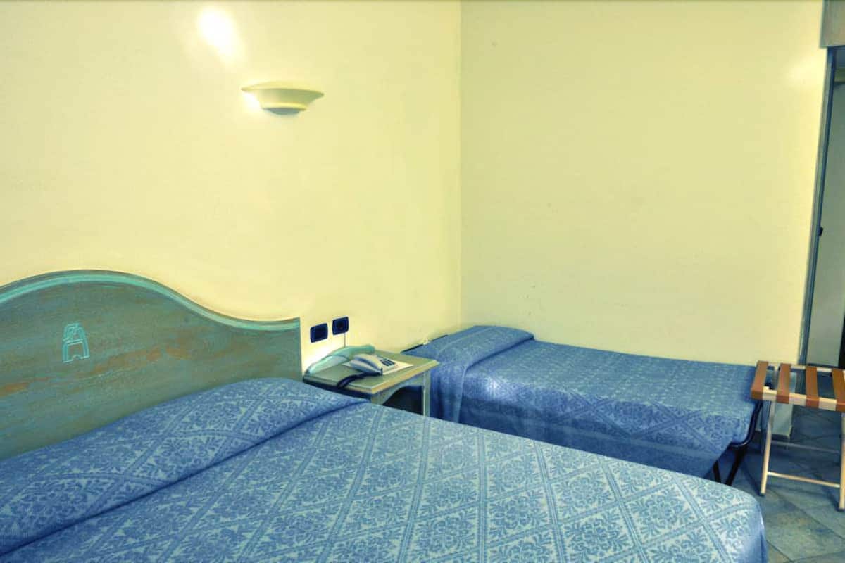 Ein kleines Hotelzimmer mit zwei Betten, einem Nachttisch, einer Lampe und einem Holzstuhl.
