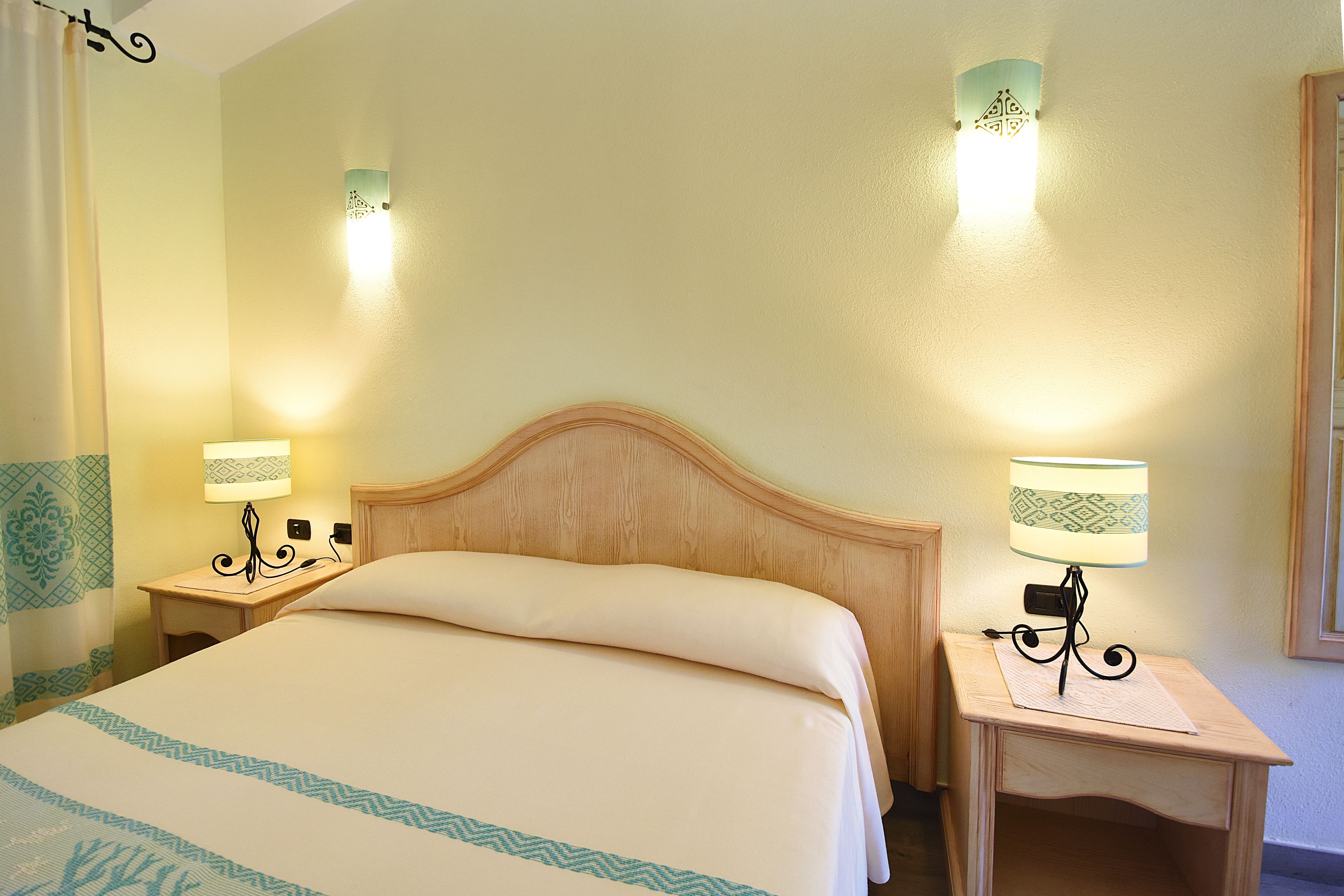 Una habitación de hotel con una cama grande, dos mesitas de noche con lámparas y apliques decorativos en la pared.