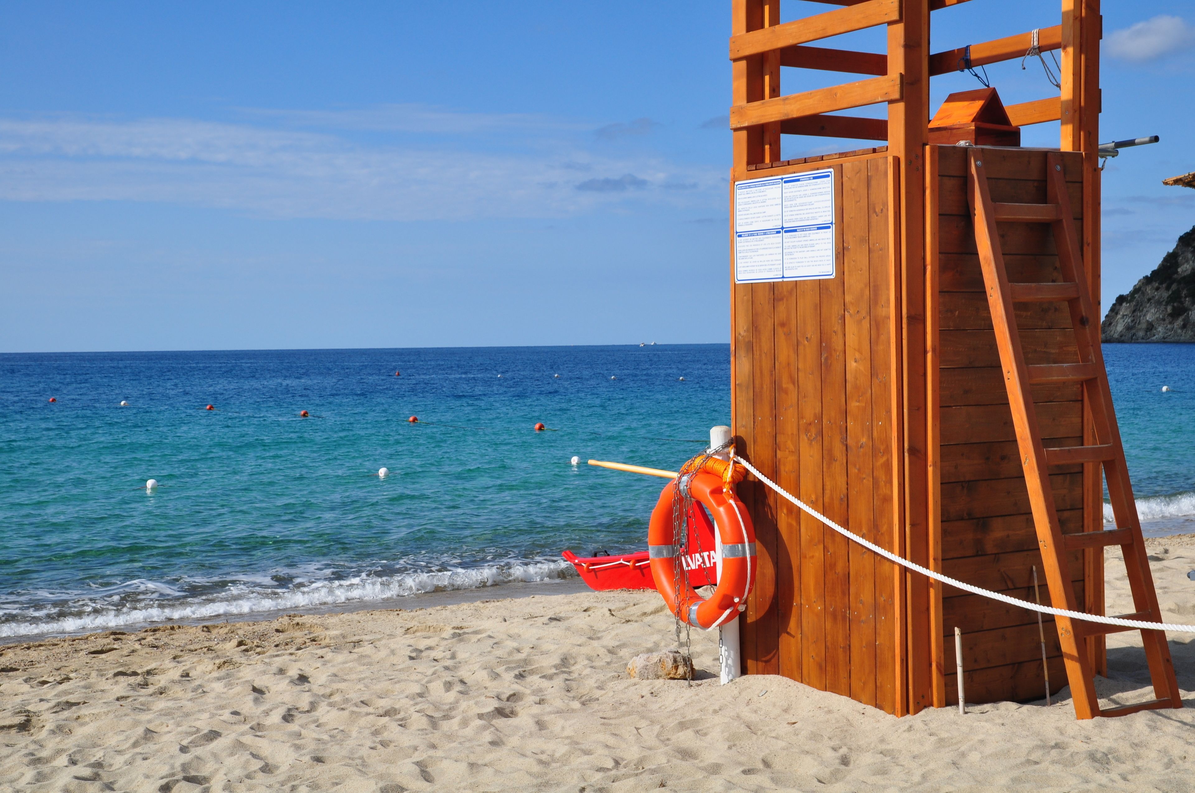 A wooden lifeguard tower with a ladder and a lifebuoy on a sandy beach.