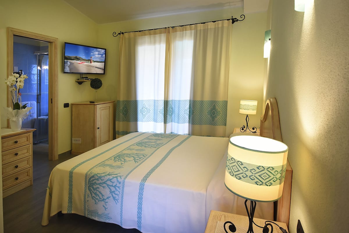 Ein Hotelzimmer mit einem Bett, einem an der Wand befestigten Fernseher, einer Lampe und einer Holzkommode.