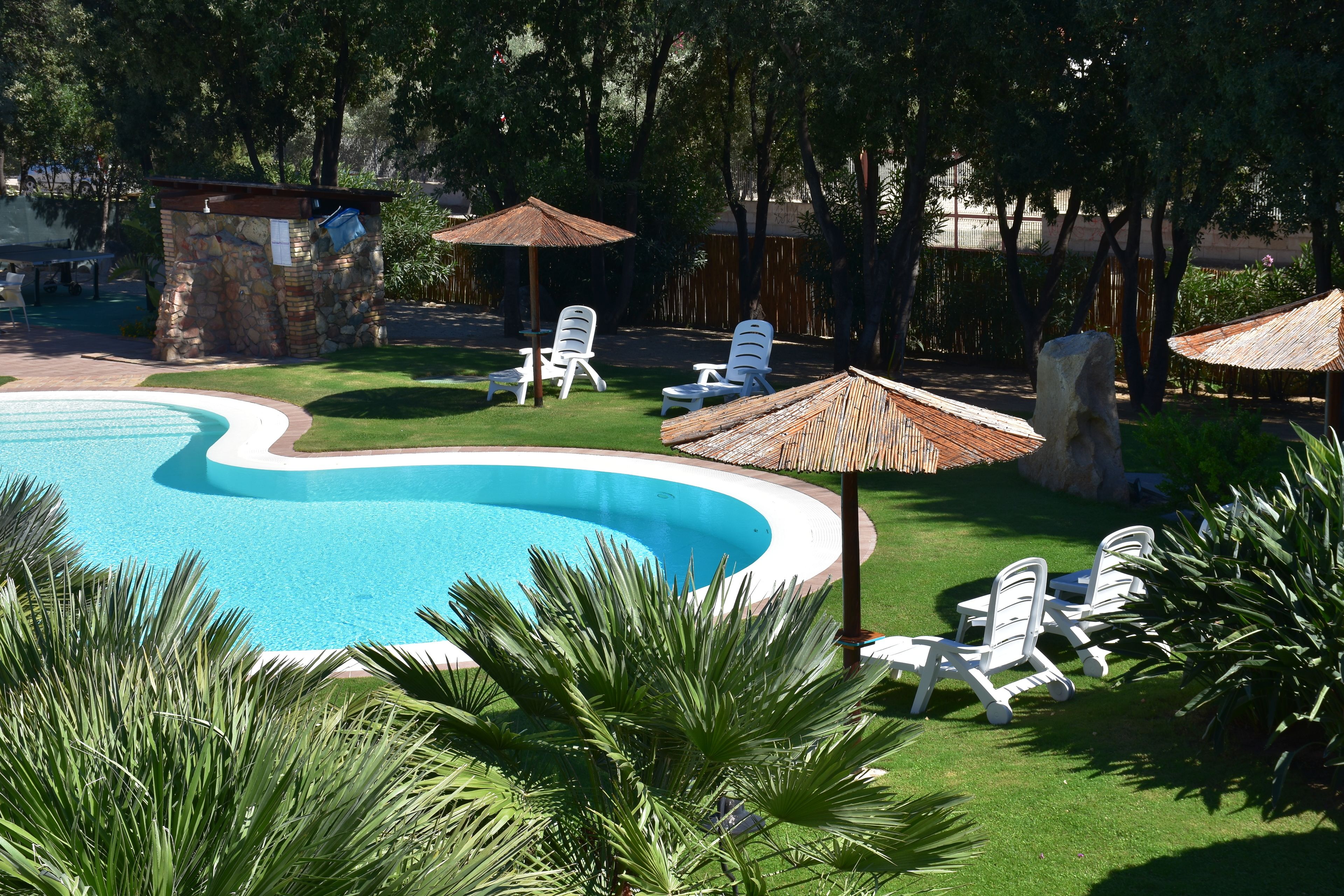 Une piscine entourée de chaises longues blanches et d’une structure en pierre.