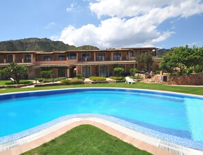 Ein großer Swimmingpool mit Fliesenrand, umgeben von einer gepflegten Rasenfläche und einem Gebäude mit mehreren Balkonen.