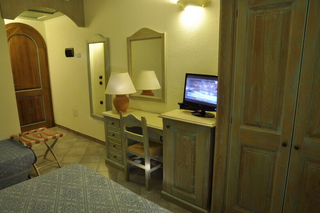 A bedroom with a bed, a desk with a computer, a chair, a mirror, and a wardrobe.