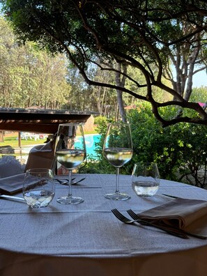 A table set outdoors with three wine glasses and cutlery, overlooking a pool and greenery.