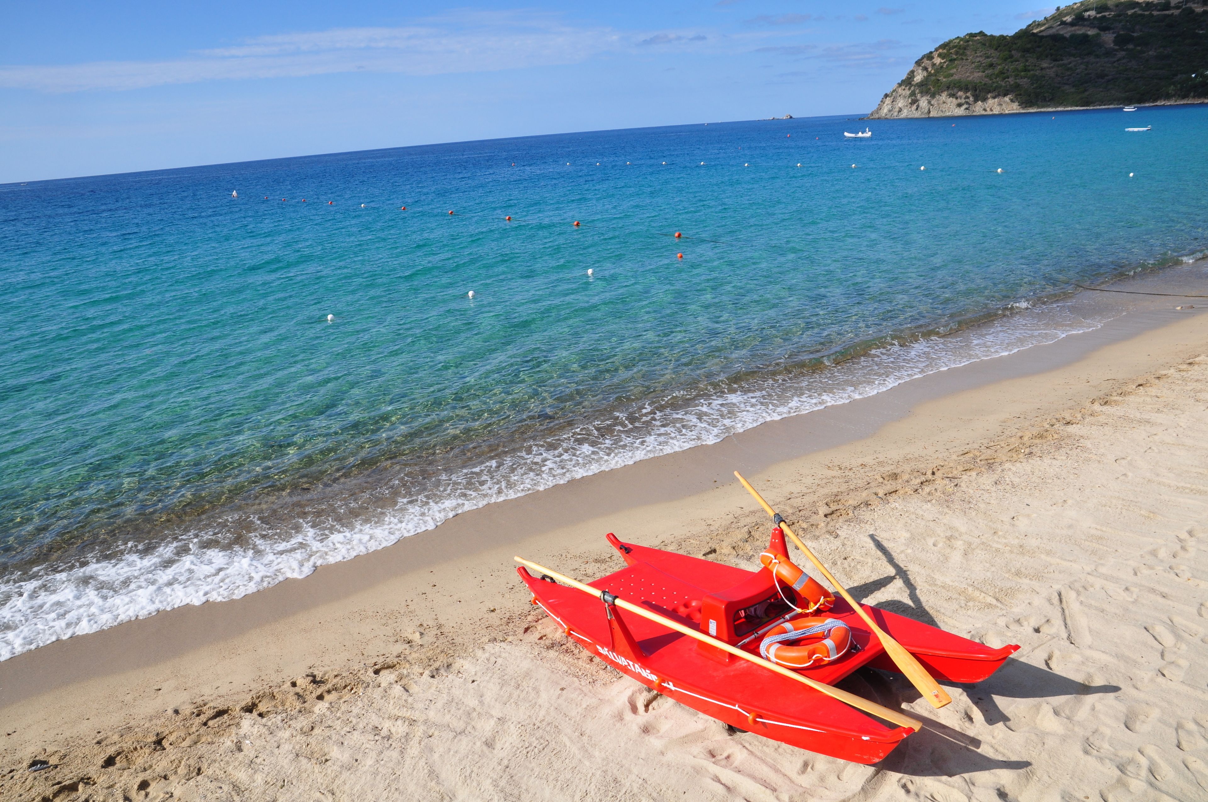 Una spiaggia con una barca rossa sulla sabbia e un mare cristallino blu.