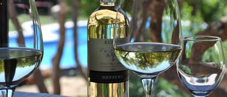 A bottle of wine and three glasses on a table with a pool in the background.