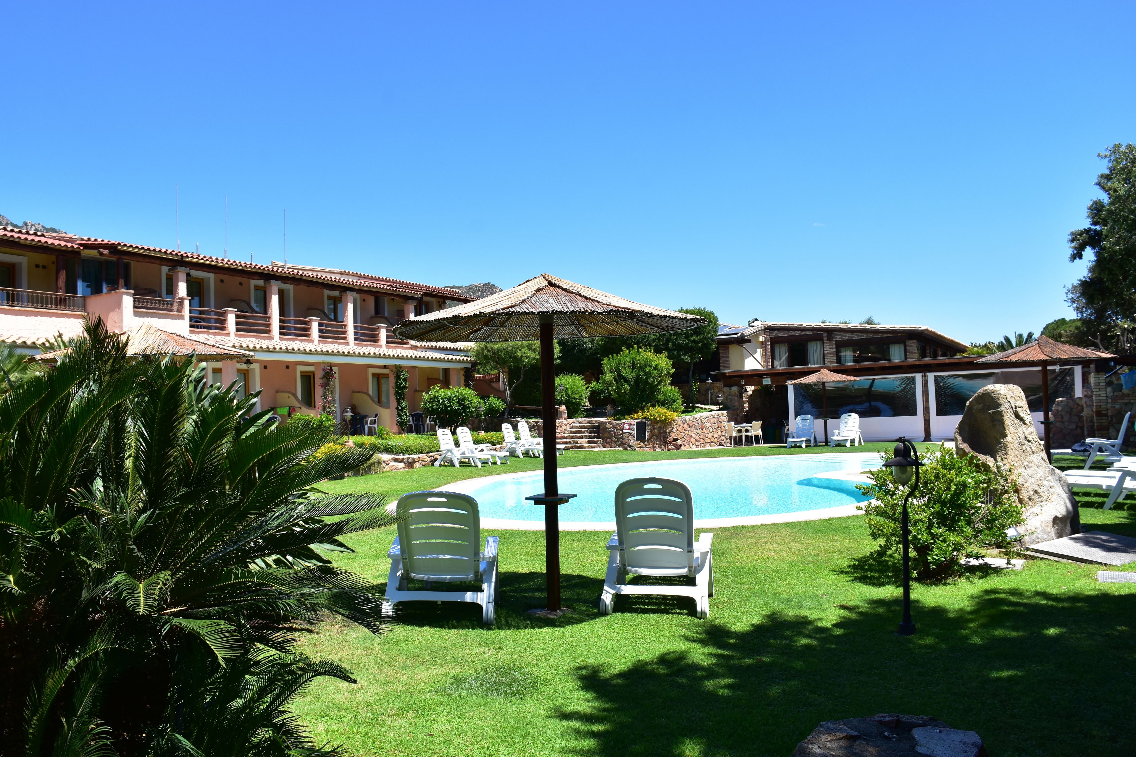 A pool area with lounge chairs, a pergola, and a large rock.