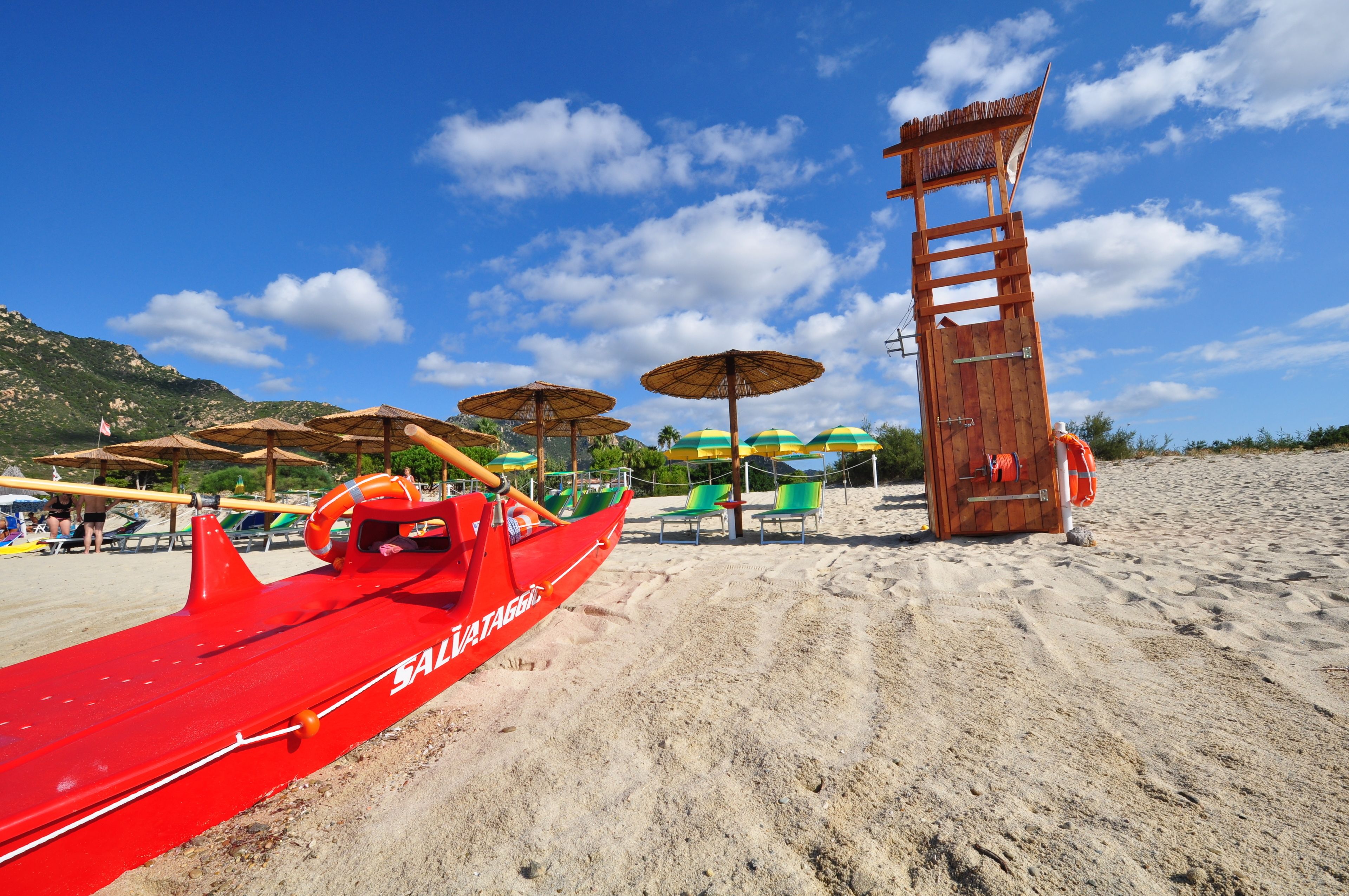 Une plage avec un bateau rouge, des parasols et une tour de surveillance des sauveteurs.