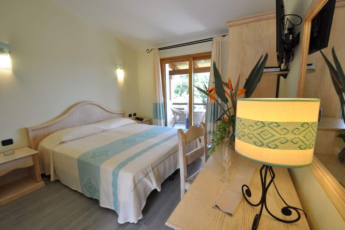 Ein Schlafzimmer mit Bett, Nachttisch, Lampe und Blick ins Freie.