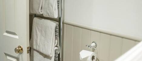 Um banheiro com um porta-toalhas com duas toalhas, um vaso sanitário com um suporte para papel toalha e três impressões botânicas emolduradas na parede.