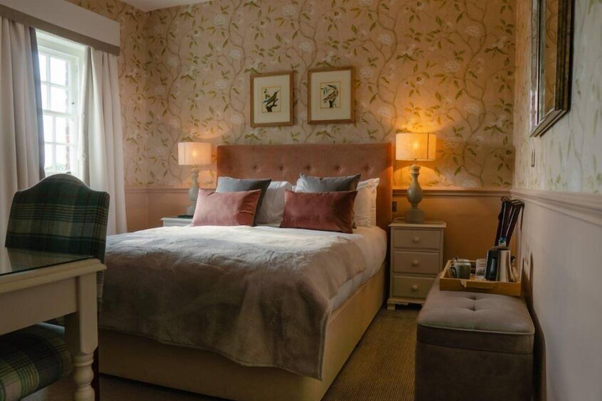 Un dormitorio ordenado con cama, mesitas de noche, una silla y una pequeña mesa.
