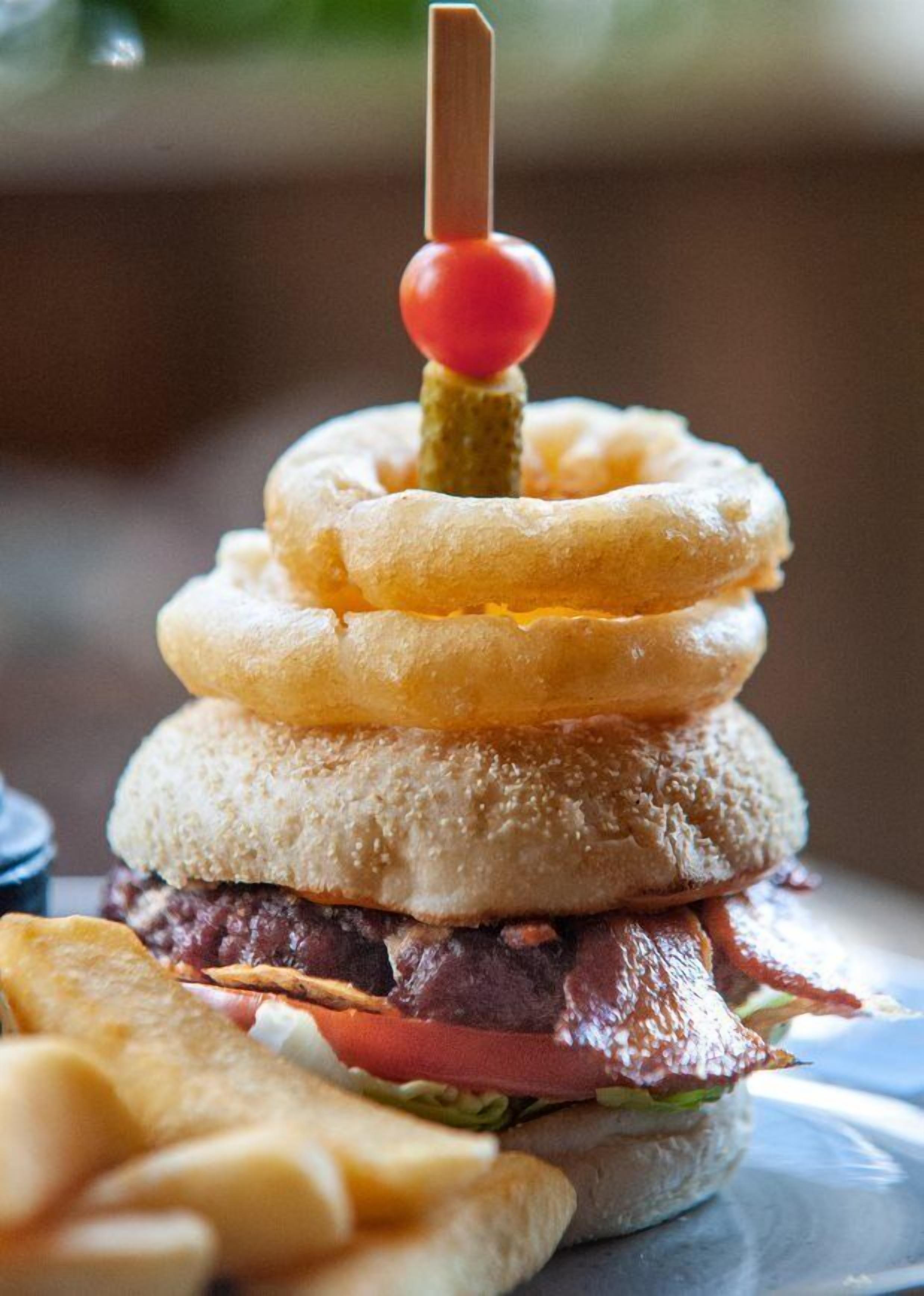 Un hamburger garni d’une pile de rondelles d’oignon et surmonté d’une tomate cerise.