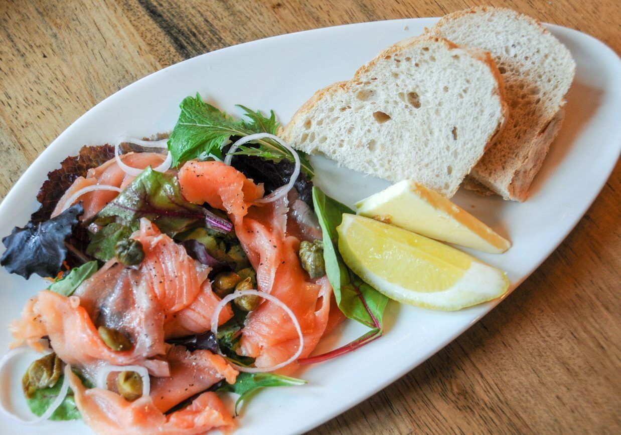 Un plato con salmón ahumado, una ensalada y rebanadas de pan sobre una mesa de madera.