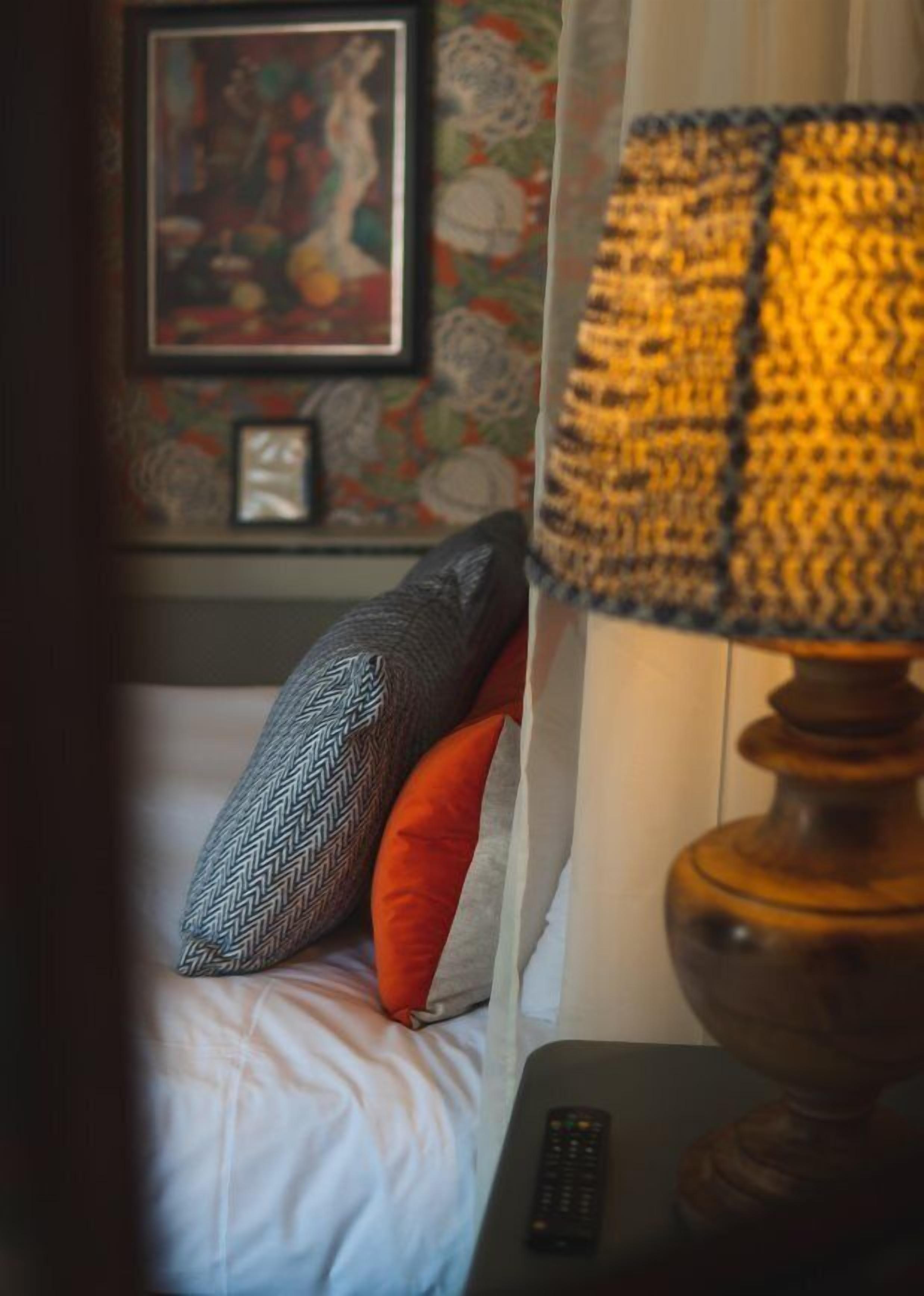 A hotel room with a bed, a remote control, and a lamp.