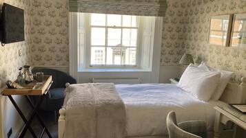 A hotel room with a bed, a desk with a chair, a window with curtains, and a radiator.