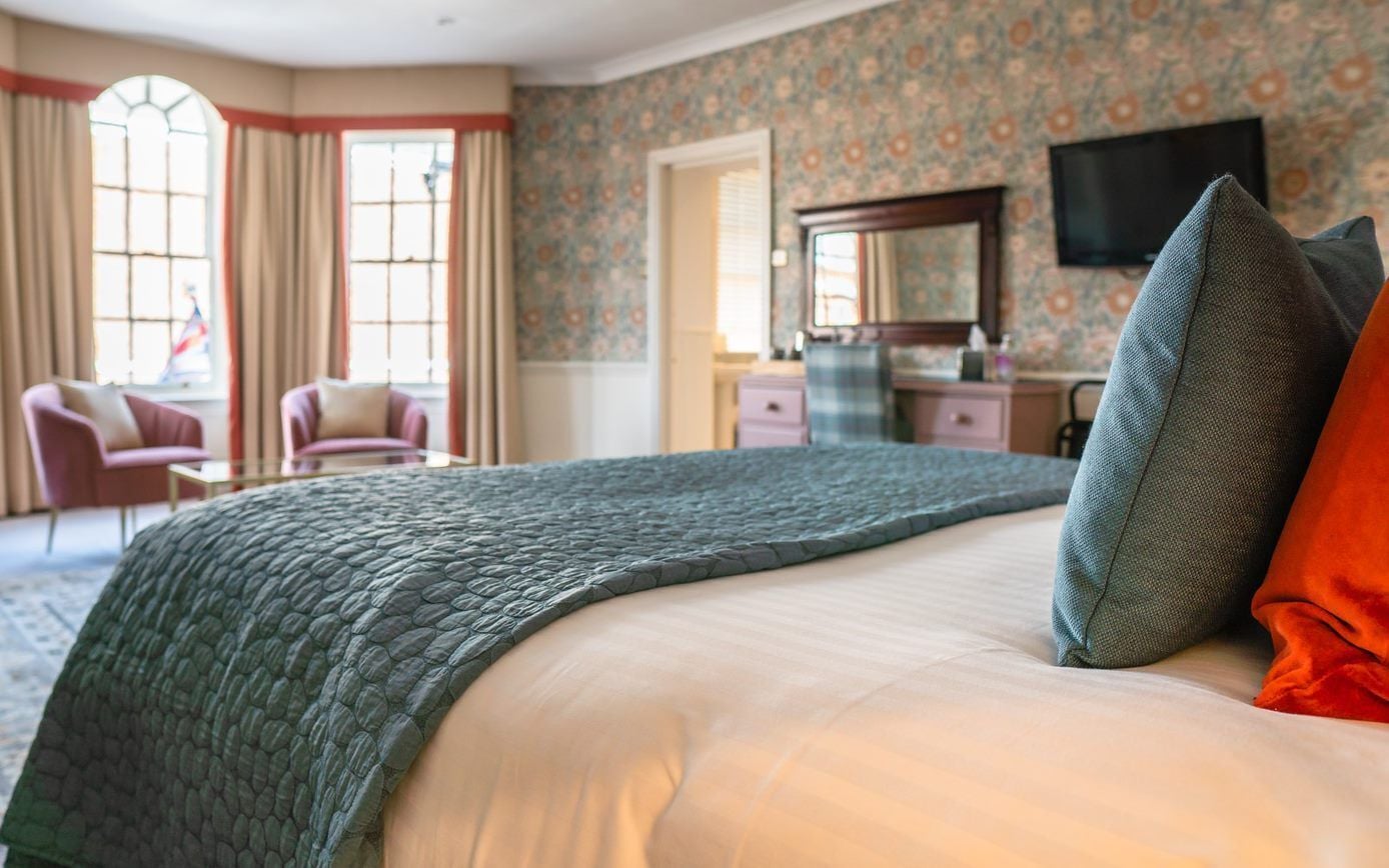 A hotel room with a large bed, a desk, and a chair. There is a window with curtains and a television on the wall.