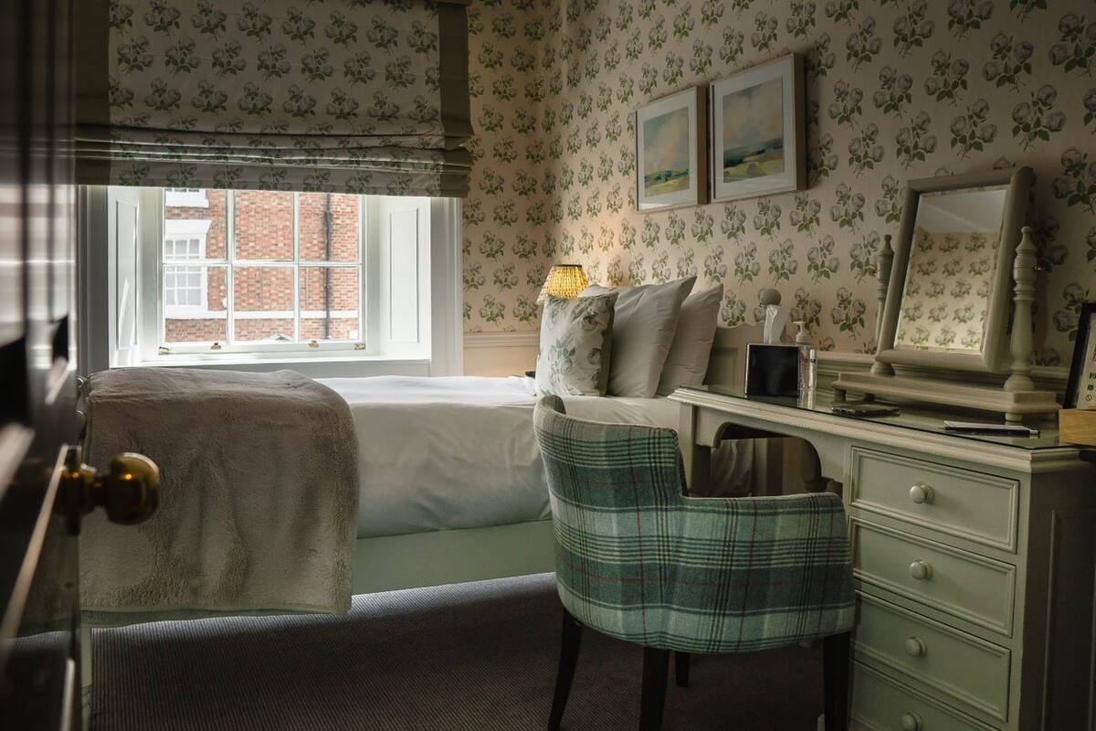 Un dormitorio con cama, escritorio, silla, ventana y espejo.