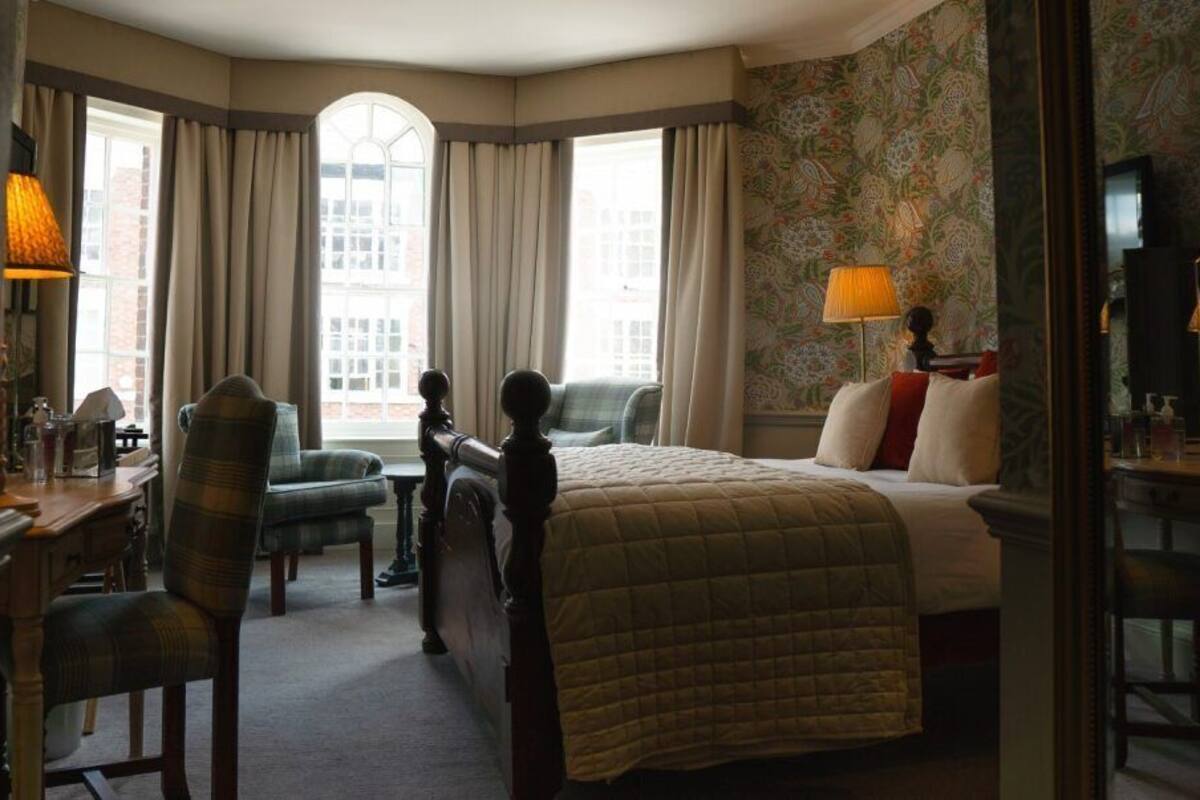 Habitación de hotel con una cama grande, un escritorio, una silla y un ventanal con cortinas.