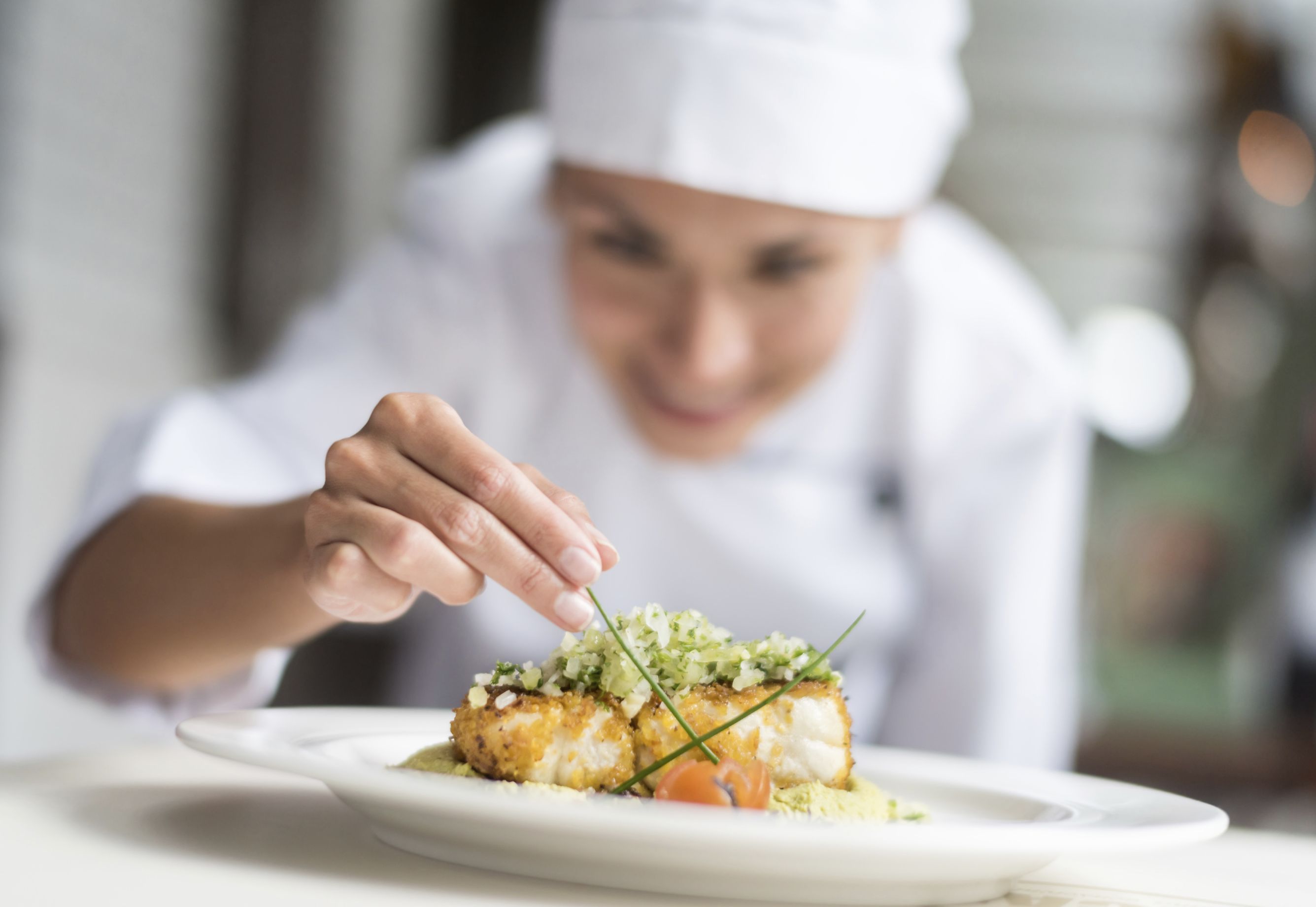 A chef preparing a dish with a white plate and garnishes.