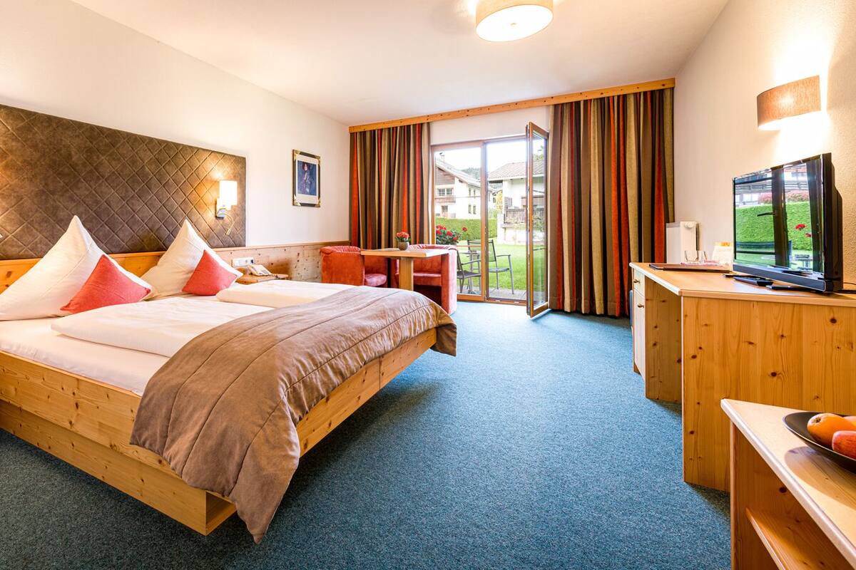 A hotel room with a bed, a desk, a television, and a view of the outdoors.