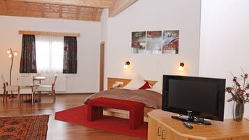 Una camera d'albergo moderna con soffitto in legno, un letto grande con biancheria rossa, una TV su un mobile in legno e un'area pranzo con tavolo e sedie.