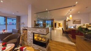 A modern living room with a stone fireplace, wooden flooring, and a glass partition leading to a kitchen area. - Hotel Goldene Rose (Lechaschau)