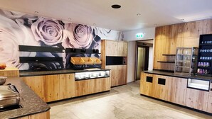 A modern kitchen with wooden cabinets, a black countertop, and a floral mural on the wall. - Hotel Goldene Rose (Lechaschau)