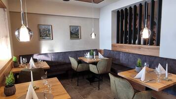 A restaurant with wooden tables and chairs, pendant lighting, and framed pictures on the walls.
