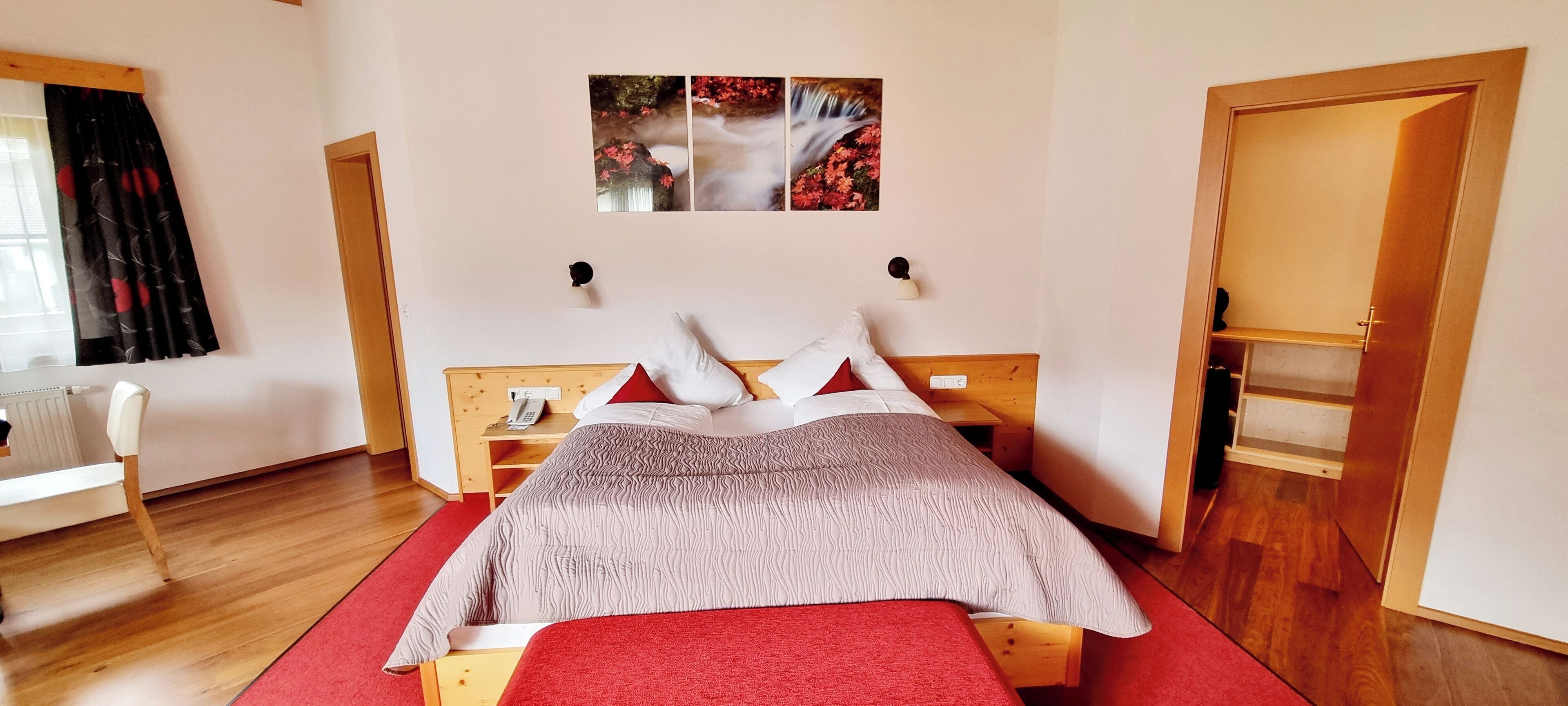 A bedroom with a wooden bed, a red carpet, a wooden wardrobe, and a wall-mounted telephone.
