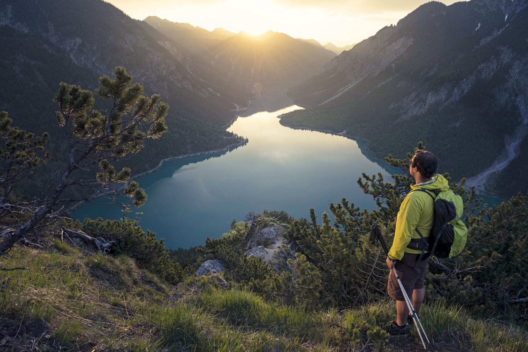Un escursionista con una giacca gialla che guarda un lago calmo circondato dalle montagne.