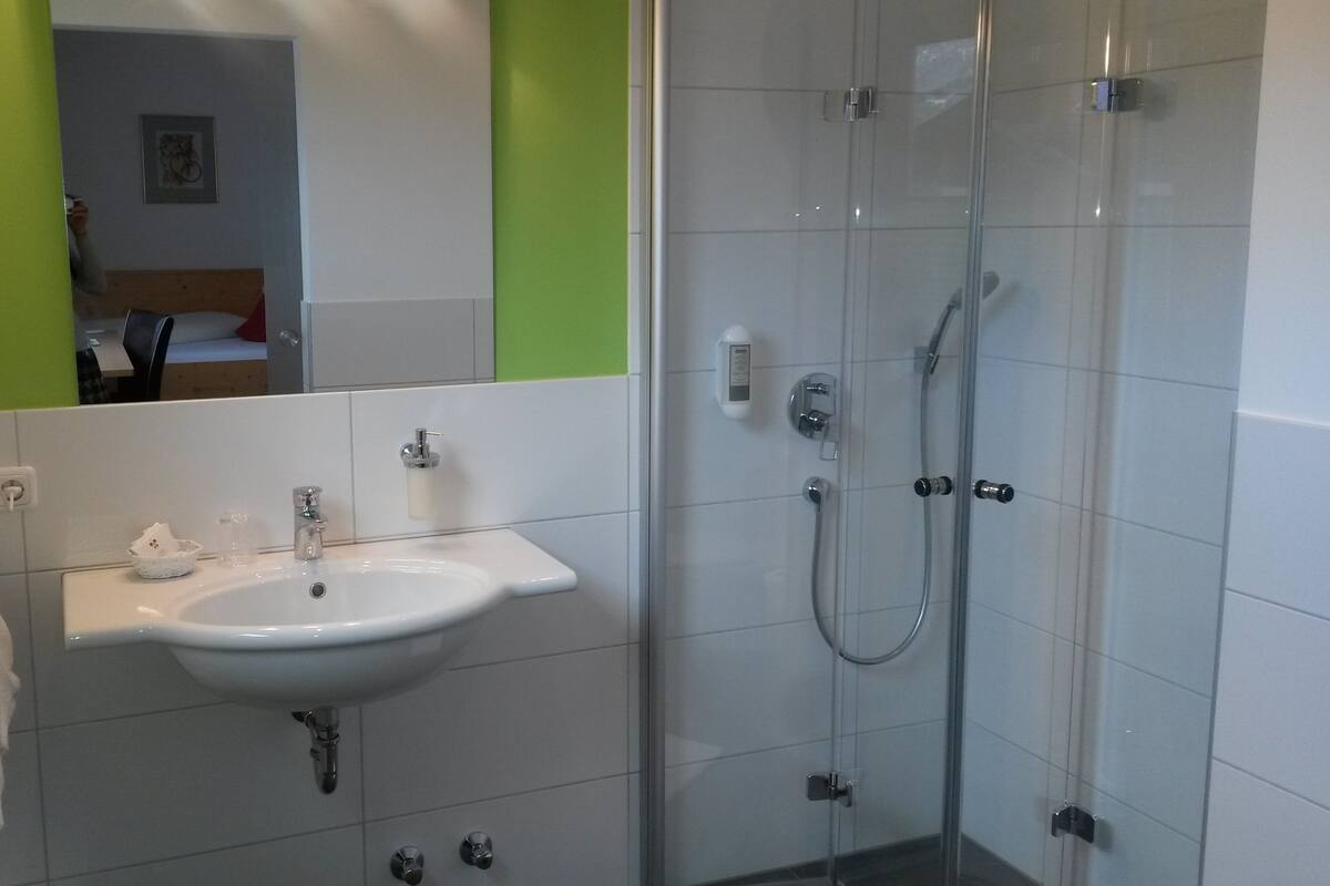 A bathroom with a sink, mirror, towel rack, and a glass-enclosed shower area.