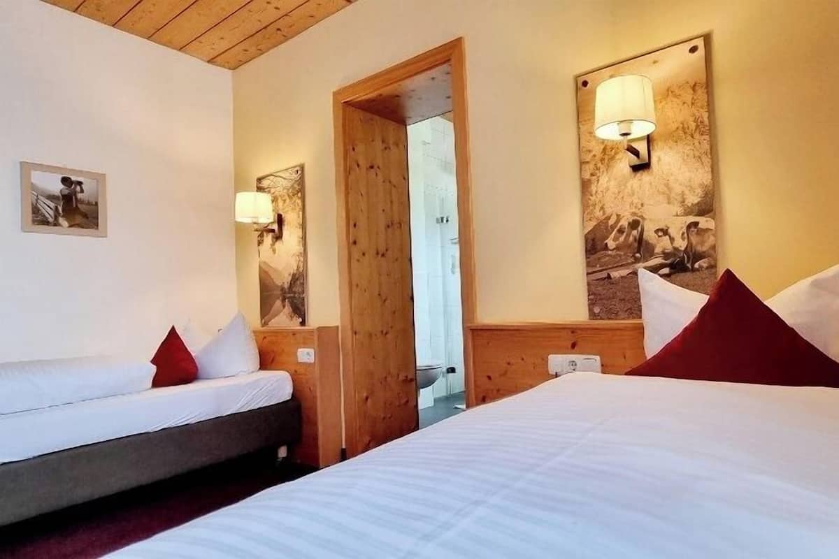 A hotel room with a large bed, a smaller bed, wooden headboard, a mirror, and a wall-mounted lamp.